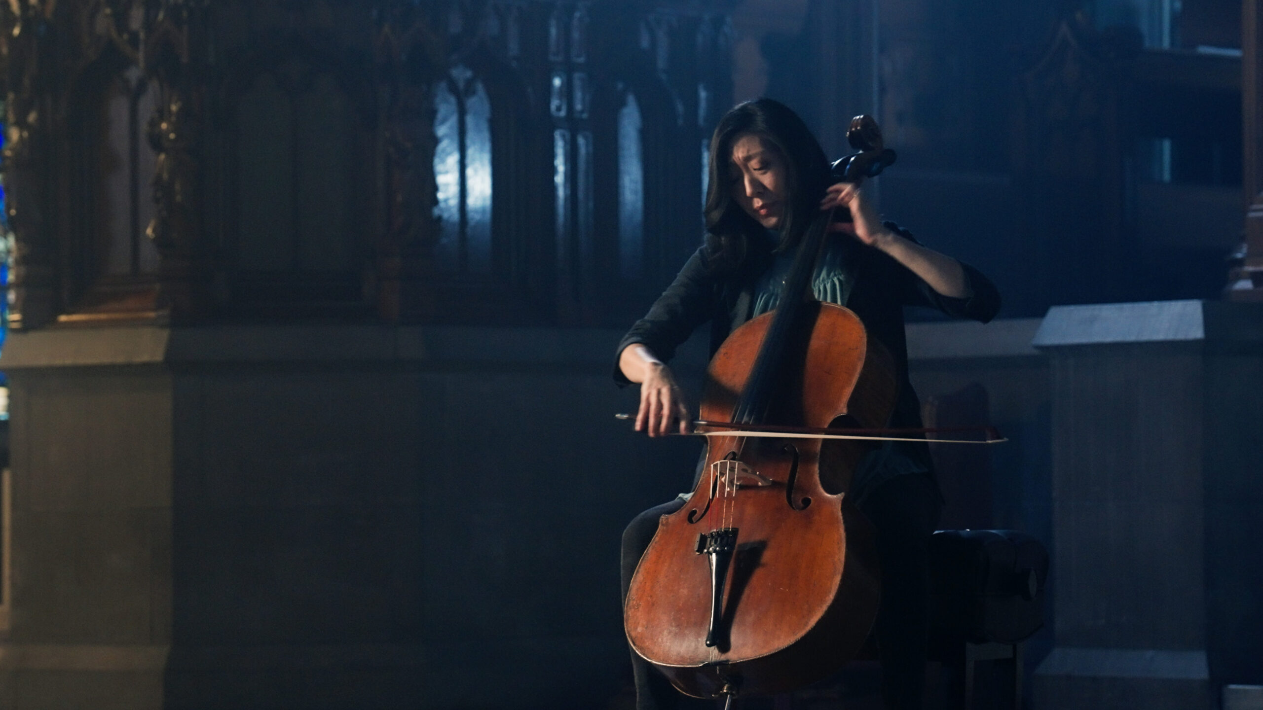 a woman plays the cello in a cinematically lit church
