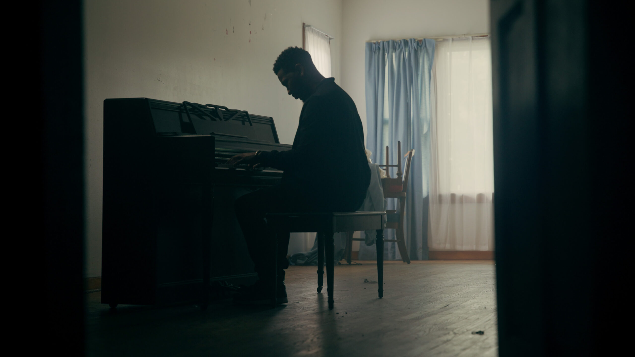 a man plays an upright piano in an empty house